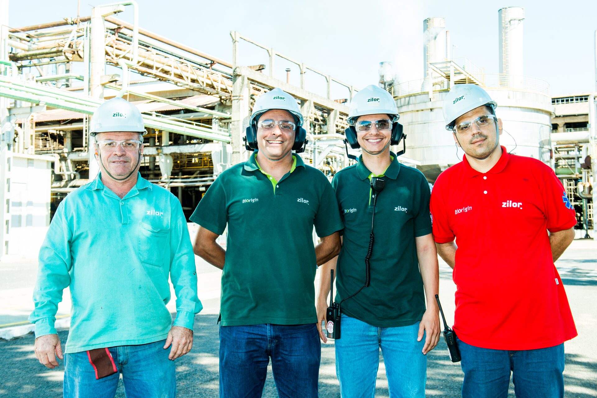Quatro colaboradores da Zilor de capacete, sorrindo, em frente à unidade industrial